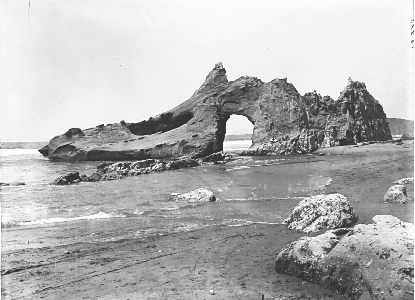 Historic photograph of a rocky outcrop on a beach near the shoreline.