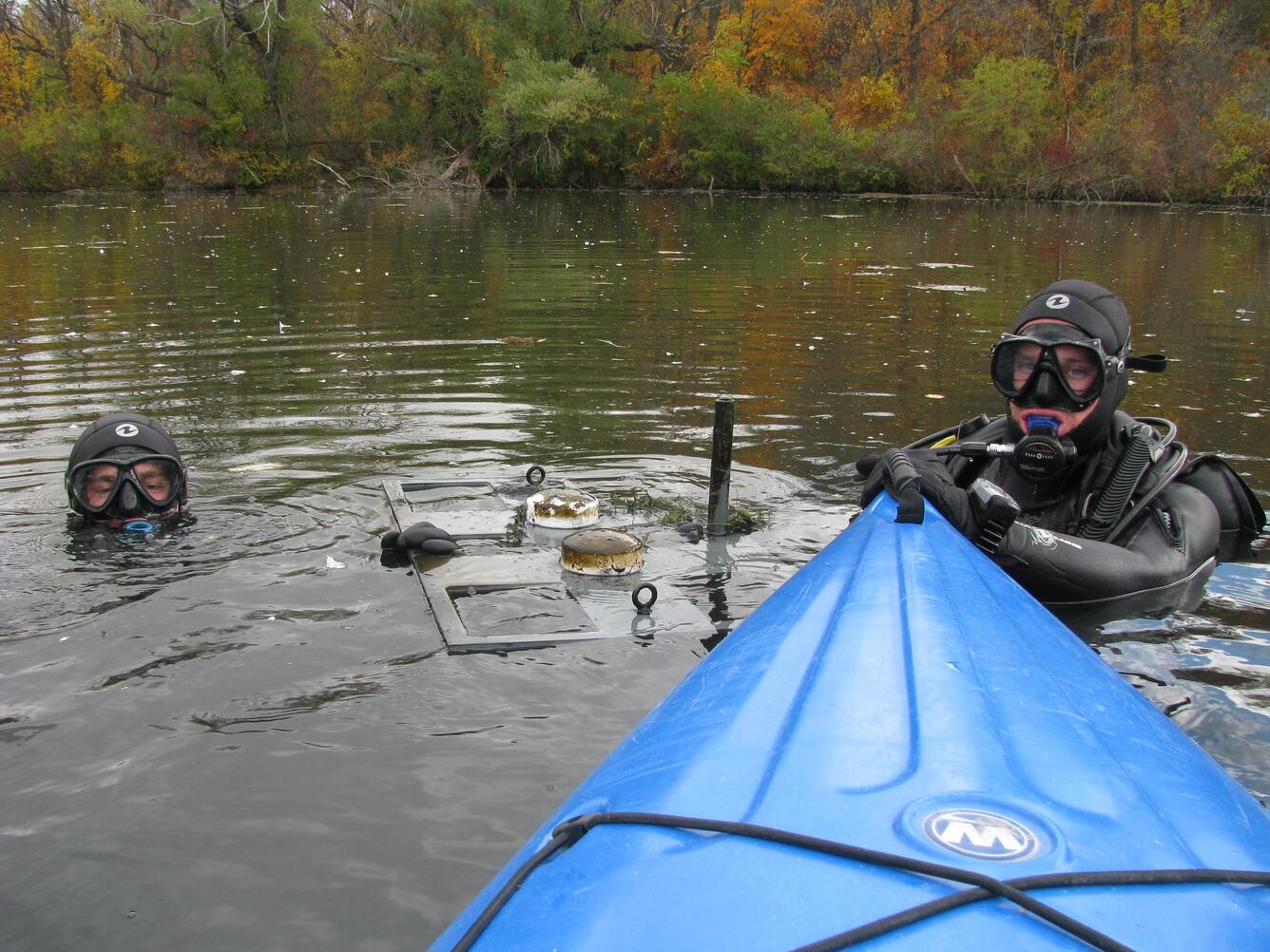 Researchers in SCUBA gear collecting sediment core samples in a pond.