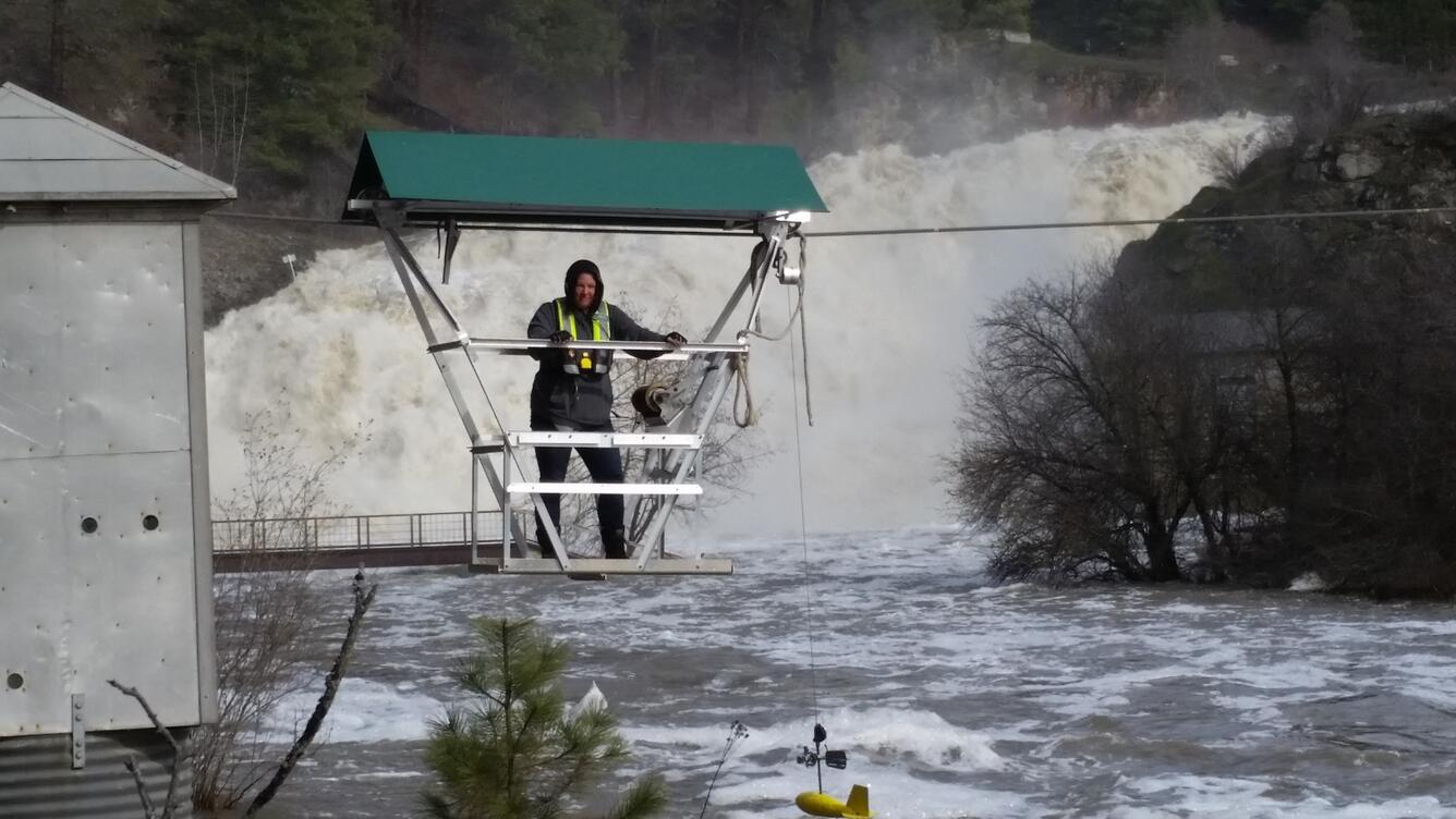 Scientist standing in streamgaging platform hanging over a river.