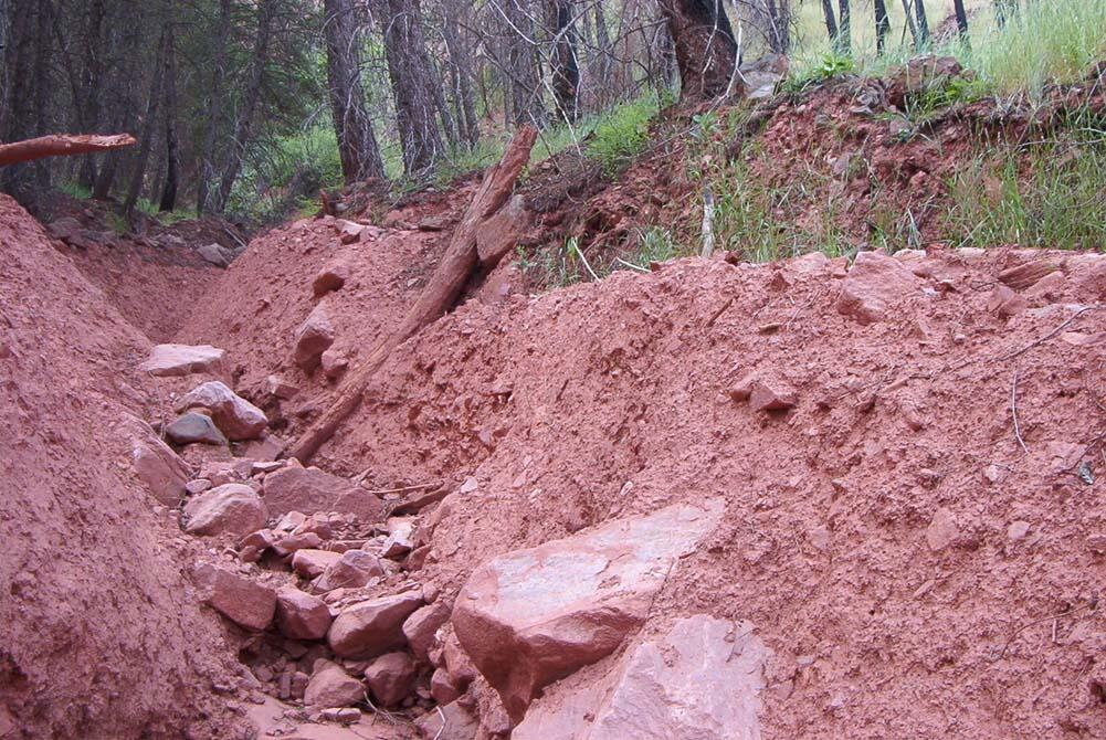 shallow trench with red dirt exposed with trees in background