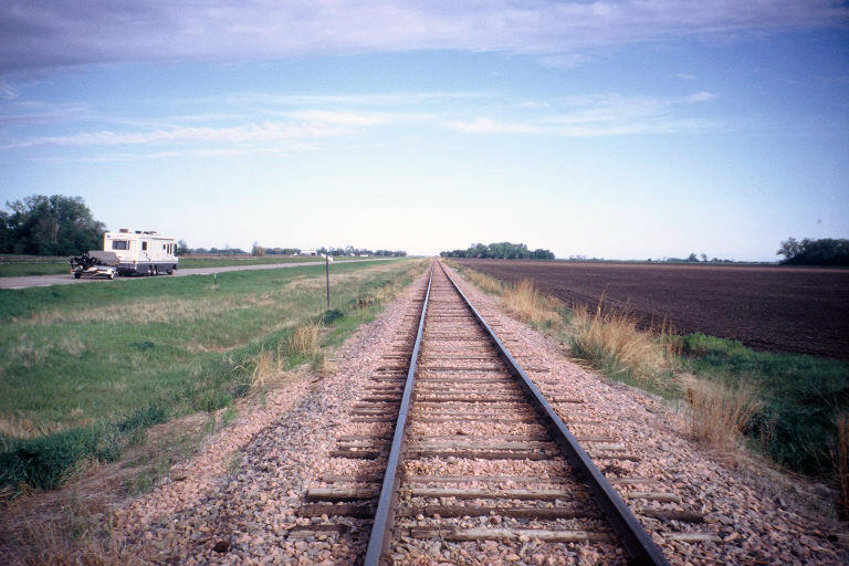 A picture of a railroad and road next to a fallow field.