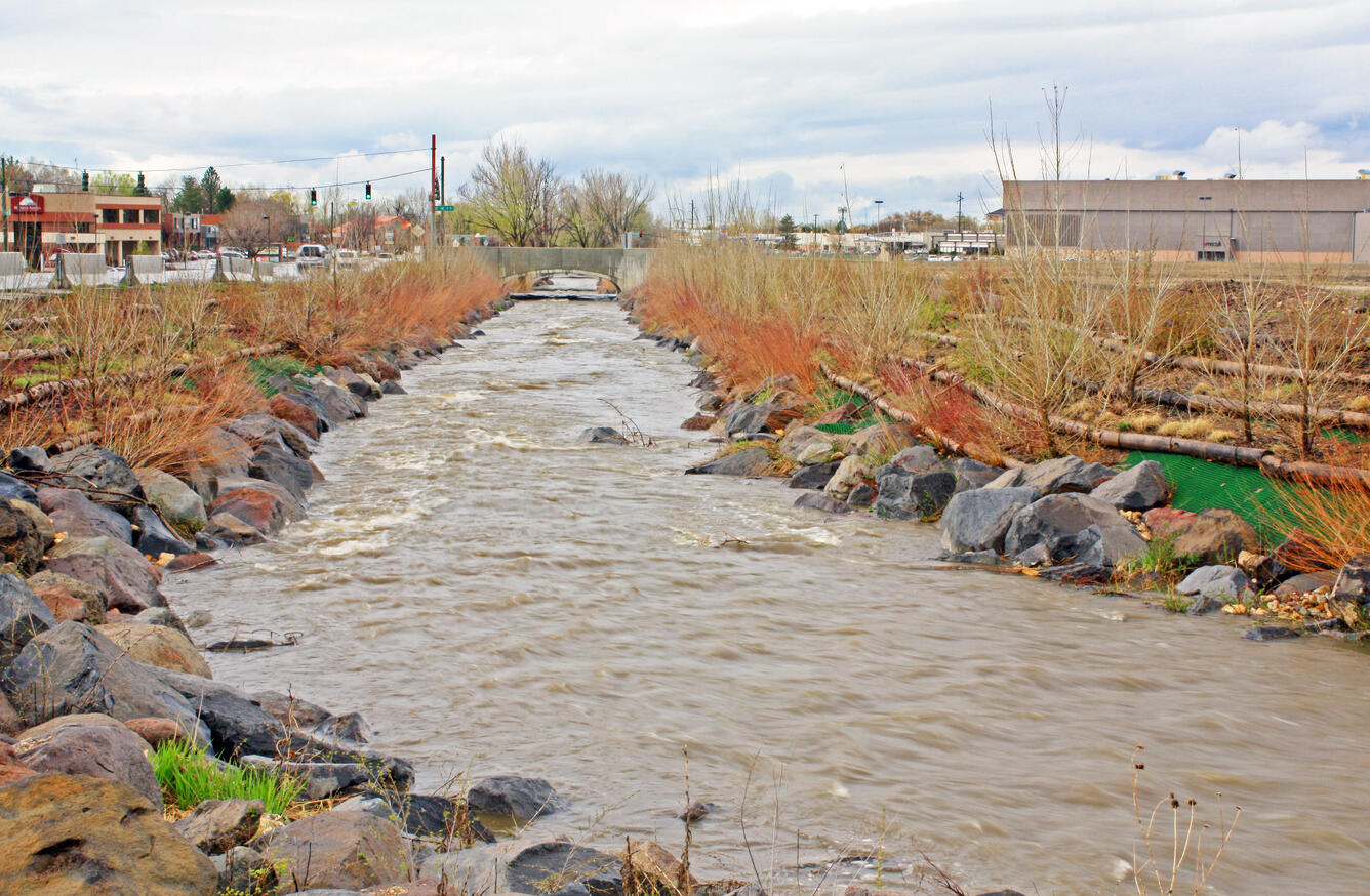 Creek with prominent bank stabilitzation work; traffic bridge and shopping centers in the background