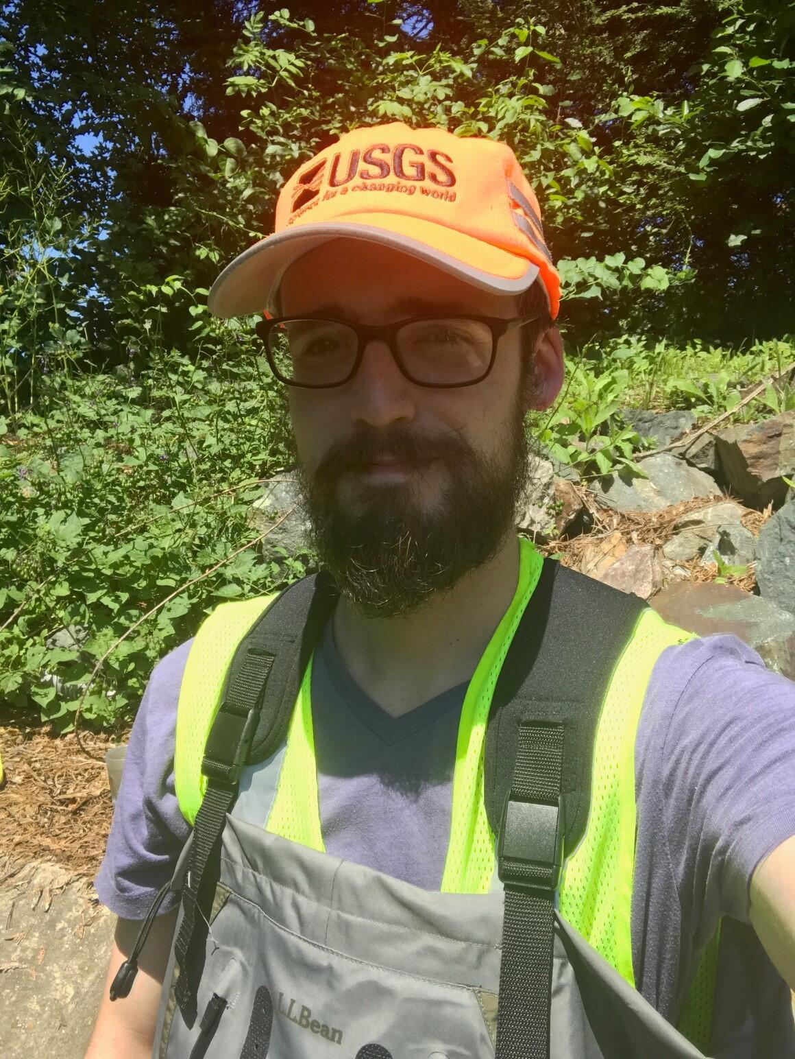 Photo of Alex Bissell standing in the field. The sun is in his eyes and he is smiling. High vis gear is everywhere. 