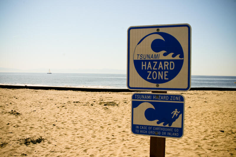 A sign at a beach warns that it's a tsunami hazard zone and that in case of earthquake to go to high ground or inland.
