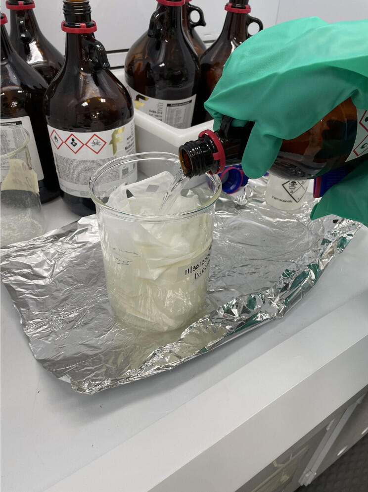 Scientist pouring a liquid chemical into a filtered beaker of dry reagent