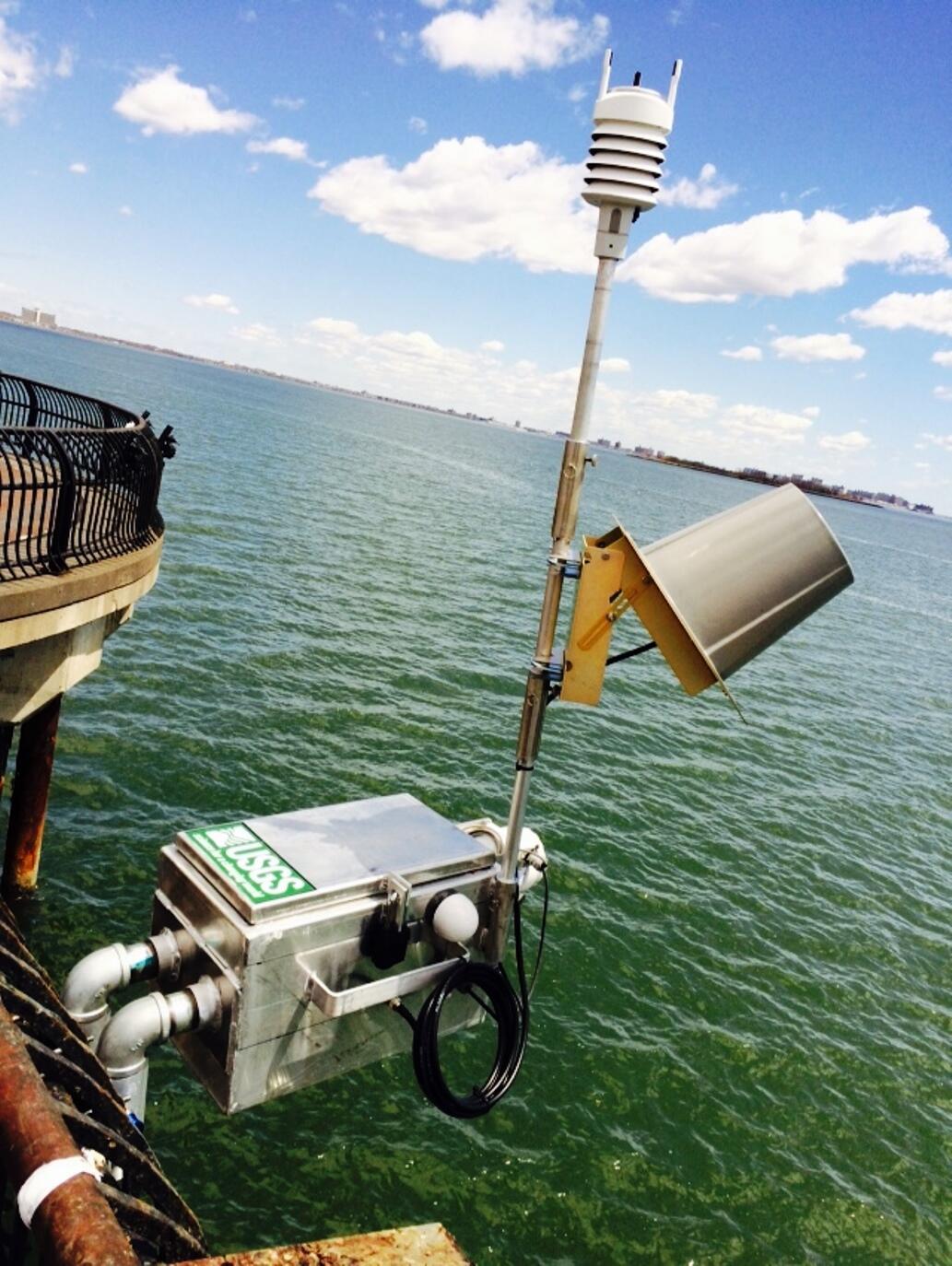 silver metal box with pole and metal hat on side of bridge by ocean