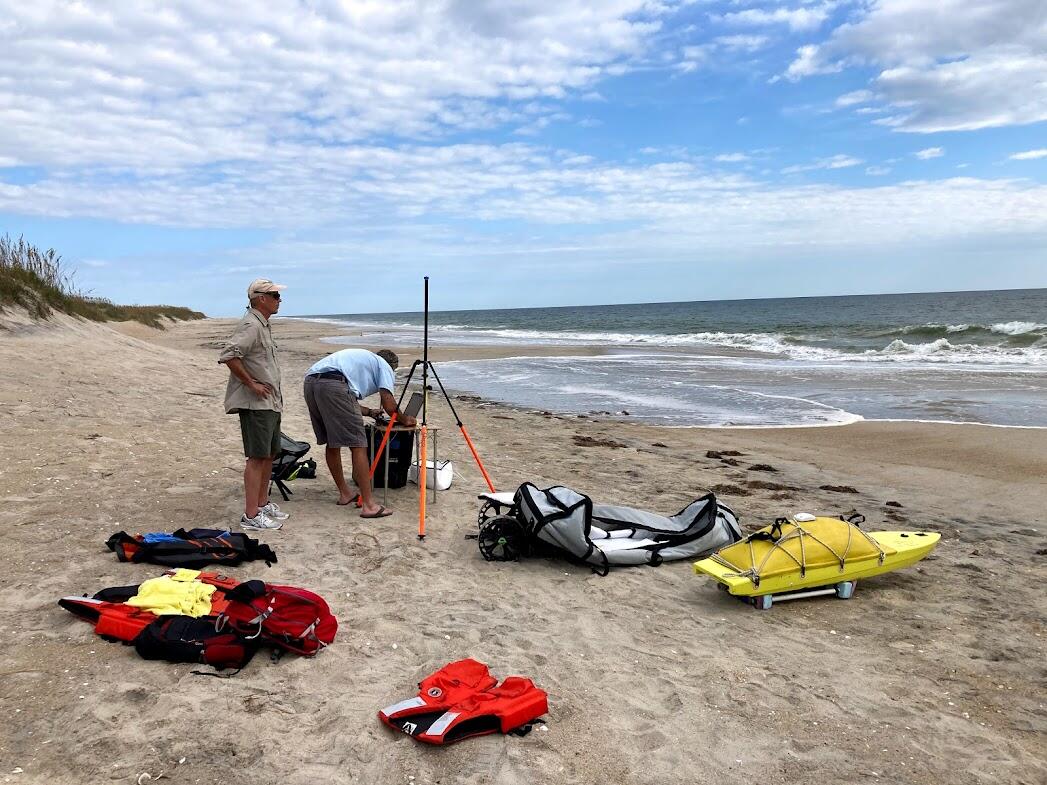 lots of colorful bags and equipment on the beach as two men look on