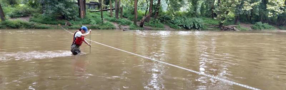 A USGS hydro tech stands in the middle of a stream to measure streamflow