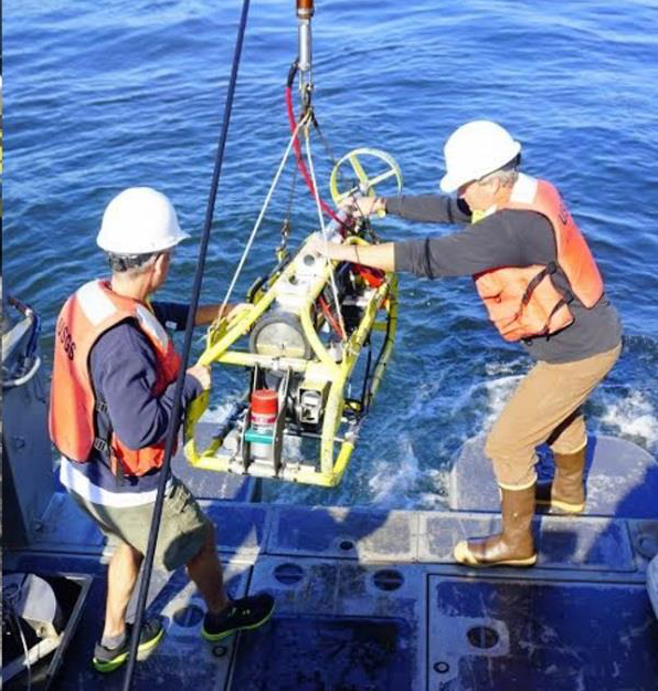 Two men wearing safety gear maneuver a metal frame carrying instruments