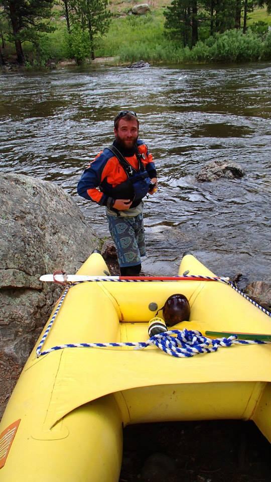 person standing in river next to an inflatable raft