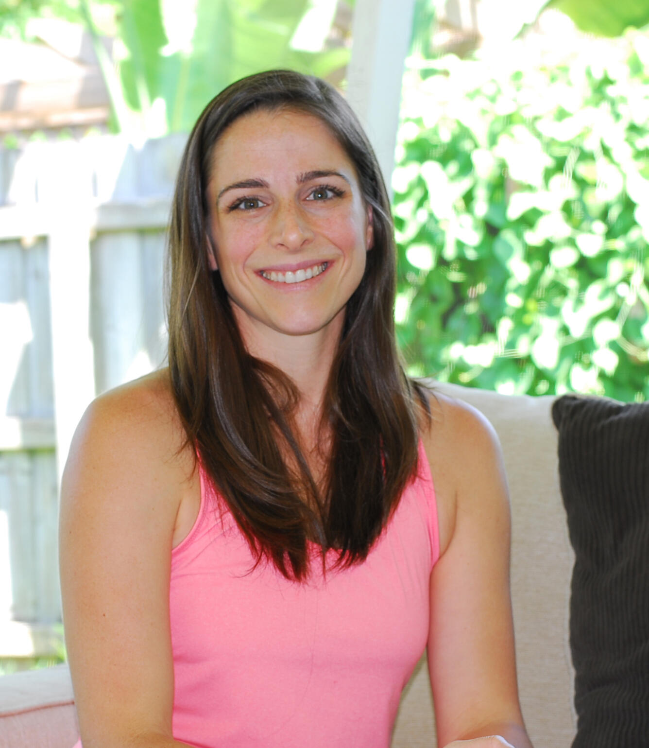 A woman in a pink dress sits in a sunny porch