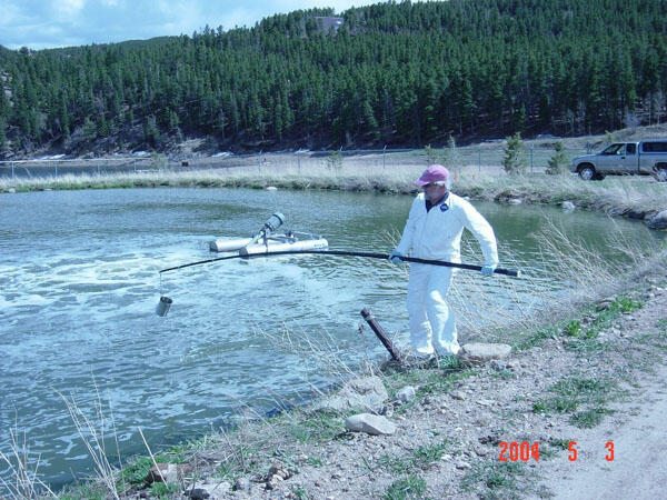 USGS scientist using a long sampling device to collect a sample of liquid from a municipal wastewater holding pond in Colorado