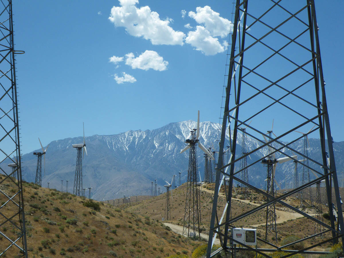 Tall windmills on a semi-arid landscape with snow-covered mountains in the background