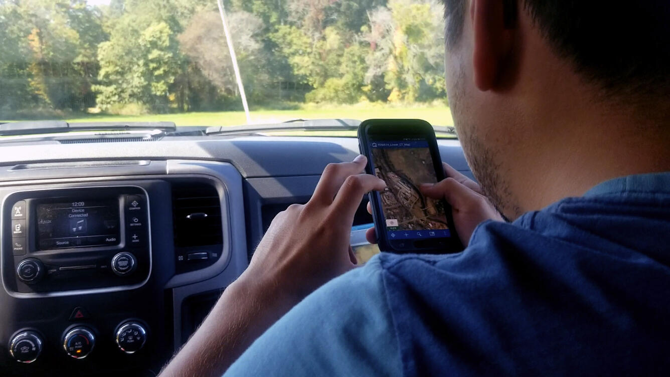 The photo is taken over the shoulder of a USGS employee as he uses the Collector App to locate the survey site.