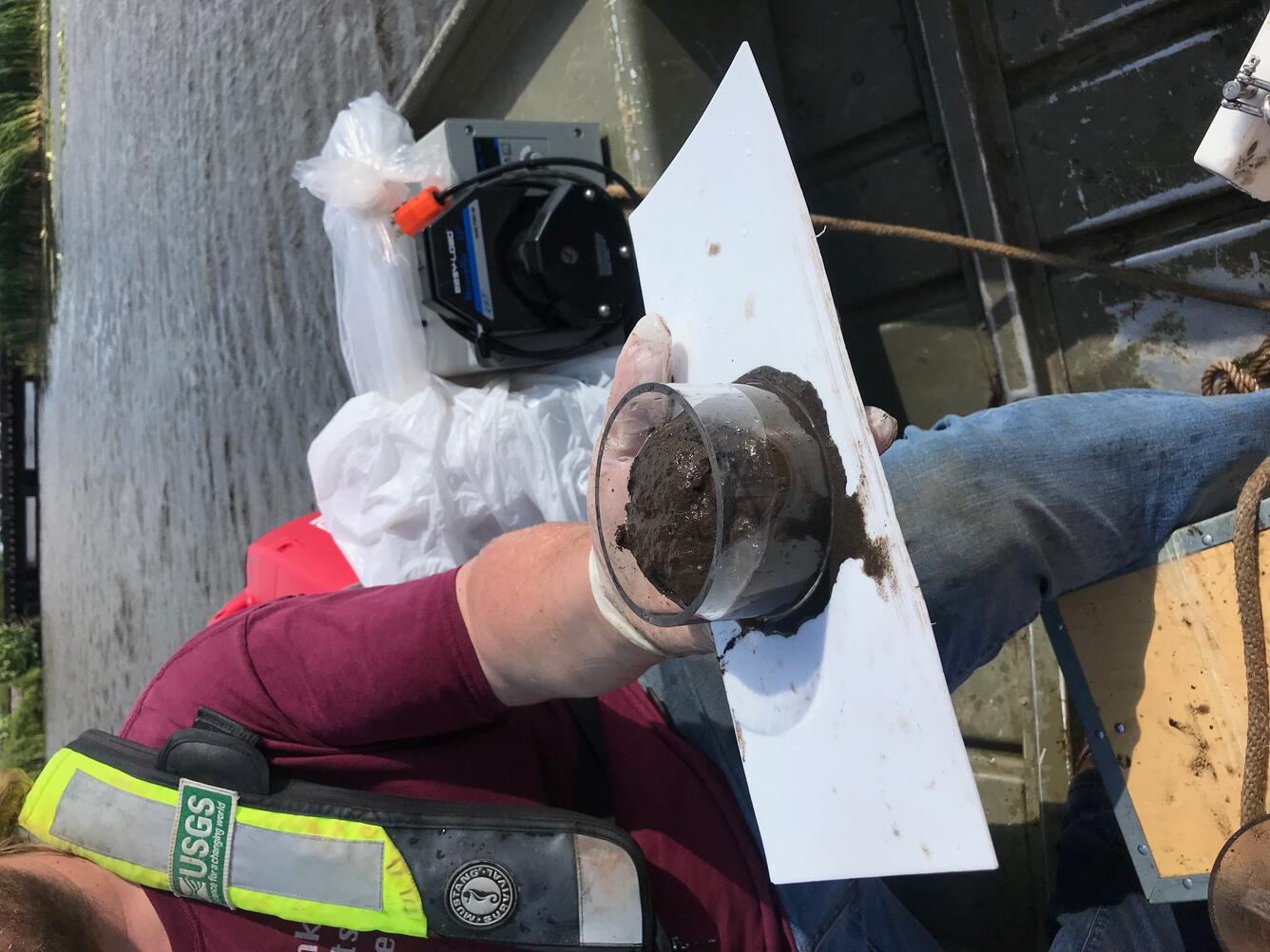 Scientist holding sediment sample while on a boat on a river.