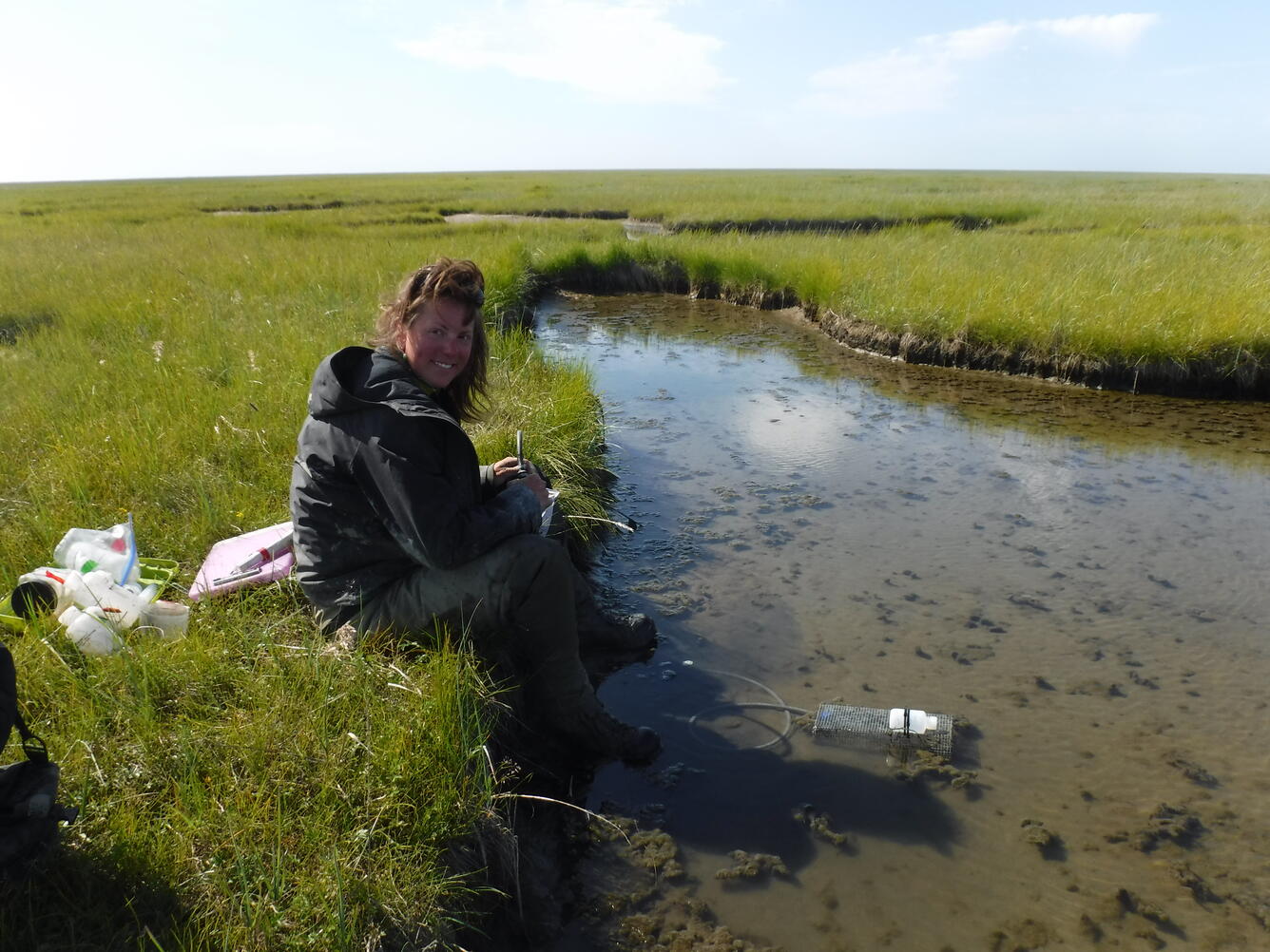 Courtney Amundson sitting on the side of a wetland creek with an invertebrate trap in the water