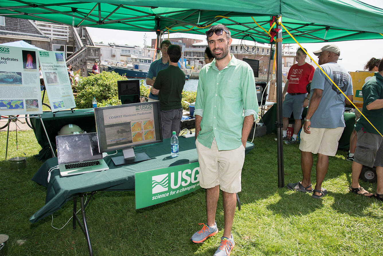 A man stands smiling for the camera, in front of a display set out under a tent at a fair.