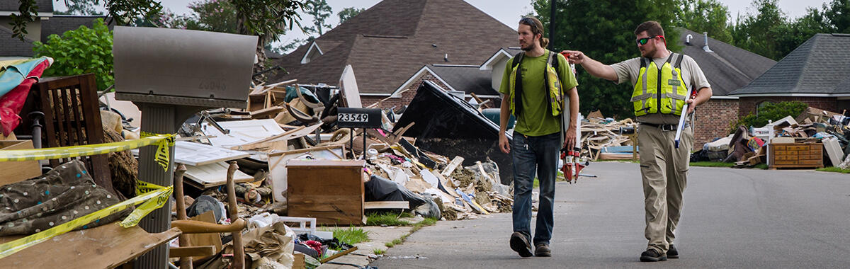 Two men walk by debris along the side of the road