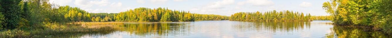 Clear blue lake with green trees in the background and blue sky with clouds reflected in the water
