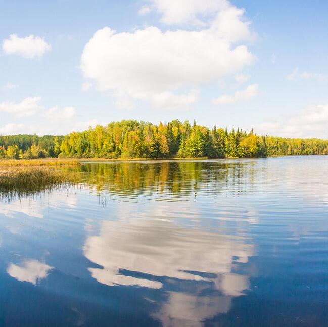 Clear blue lake with green trees in the background and blue sky with clouds reflected in the water