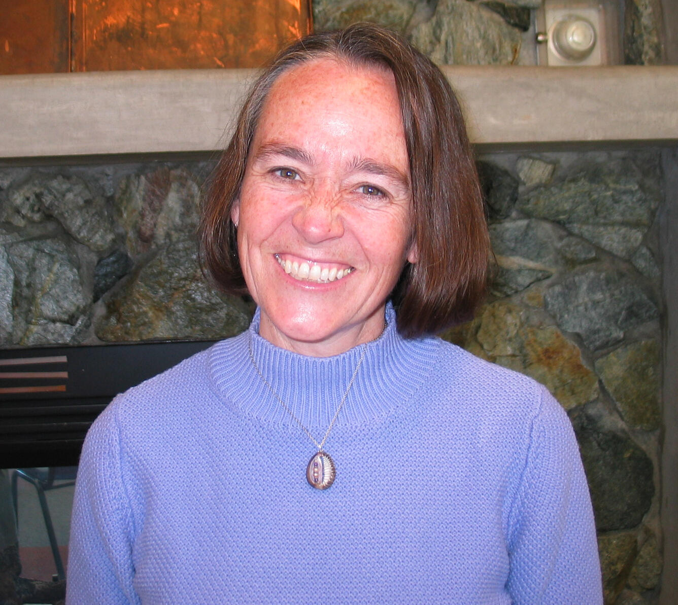 Dede Bohn standing in front of a fireplace 