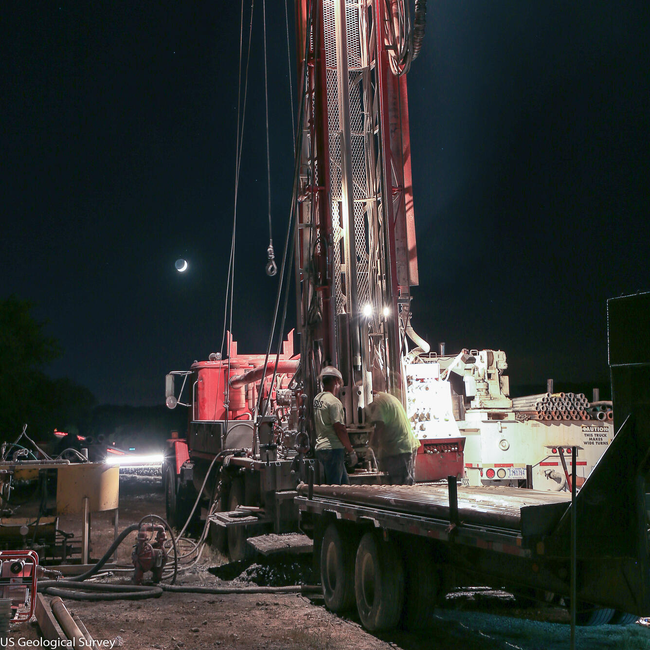 Image shows USGS scientists standing beside a drill rig in protective gear.