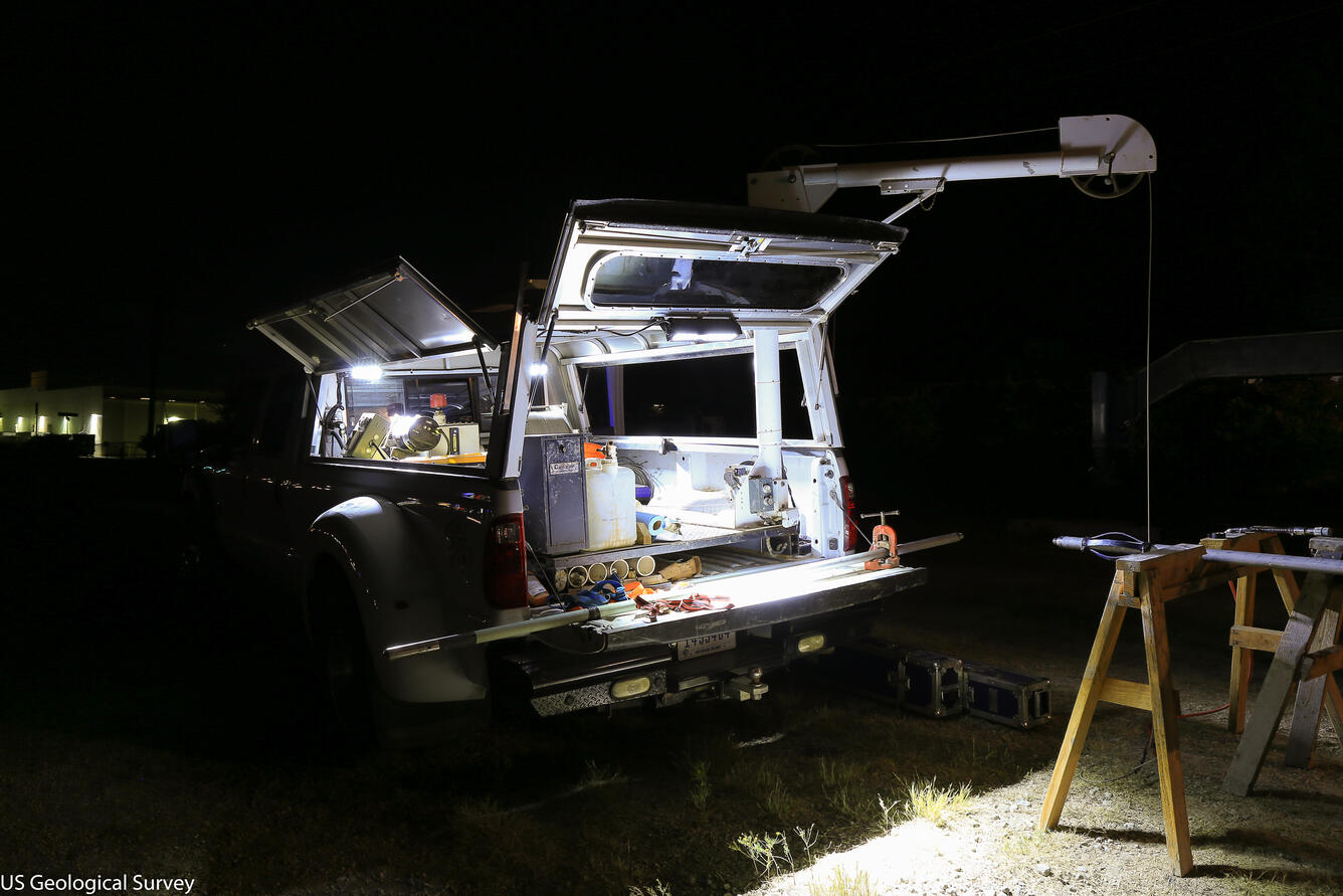 A vehicle is shown at night, with its trunk open and floodlights on