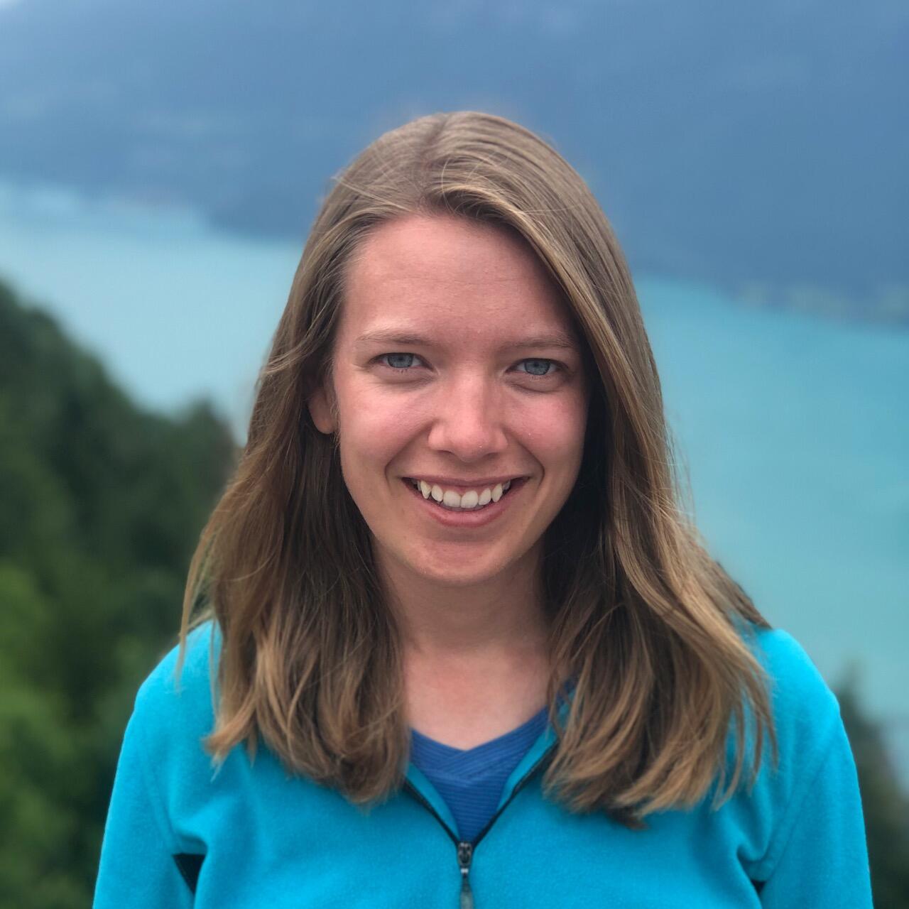 Staff photo of Emily Wilkins, Social Scientist, in front of a green and blue background, wearing a blue sweatshirt. 