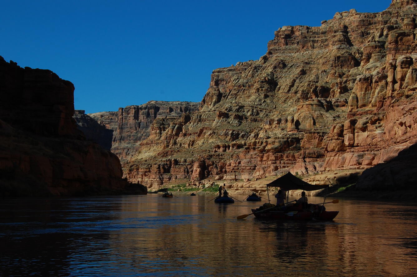 The black silhouettes of the SCREE flotilla drifts in the shadow of rock walls within Narrow Canyon of the Colorado River.