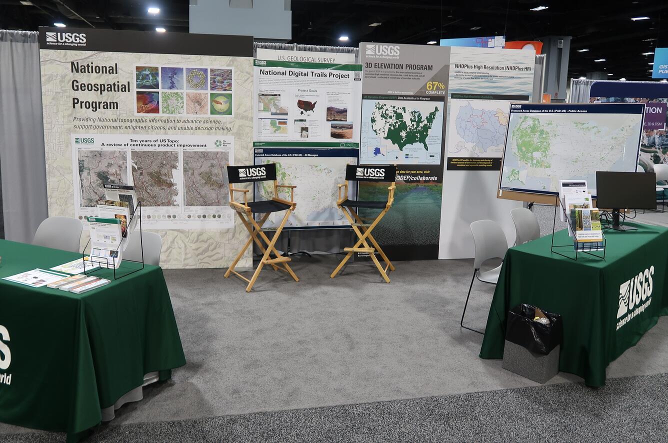 Conference exhibition booth with two tables topped with fliers in front of some large display graphics.