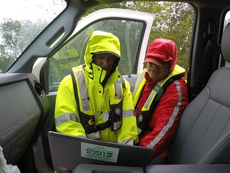Image shows two USGS scientists looking at a computer screen in a truck
