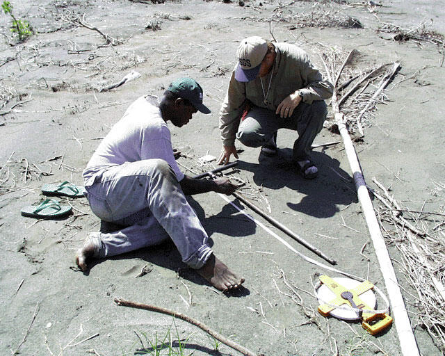 Two men examine a long thin core of sediment they just drew out of the ground.