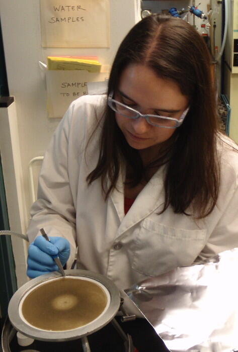 USGS scientist lifting a filter caked with sediment that's on top of a filter plate used for filtering suspended sediment 