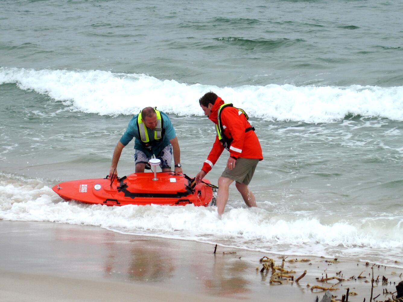 two men pulling orange ADCP craft onto beach