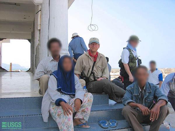 A man in a baseball cap and red bandana sits on steps with a small group of people of different nationalities