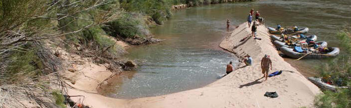 Boats with people disembarking onto a large sandbar with an eddy in the Colorado River