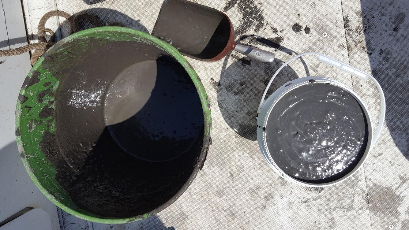 2 buckets with gray mud in them and a trowel on a board deck