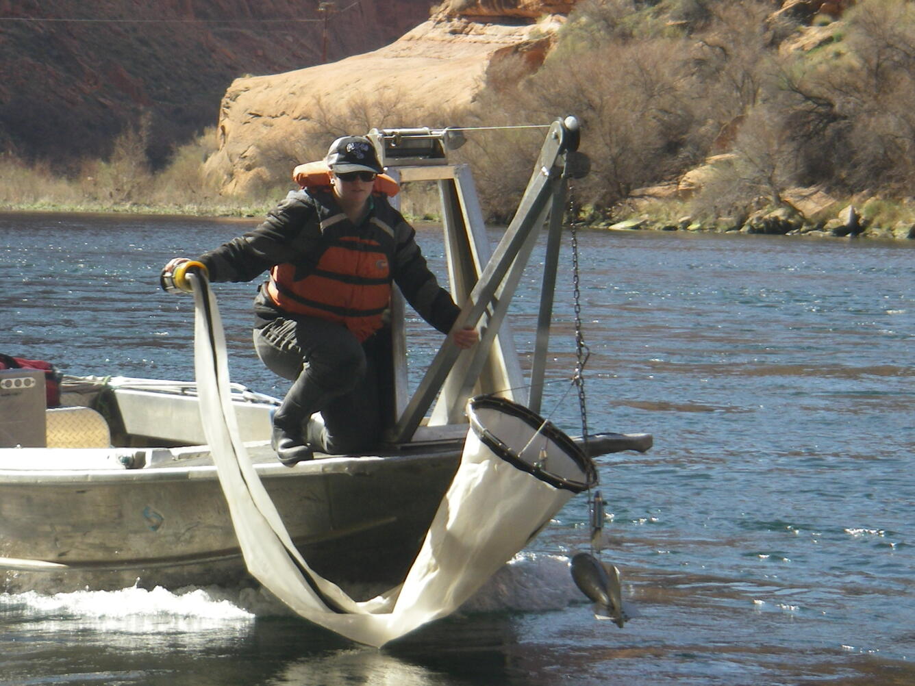 USGS researcher on small boat holding the end of a net used to capture insects in the water.