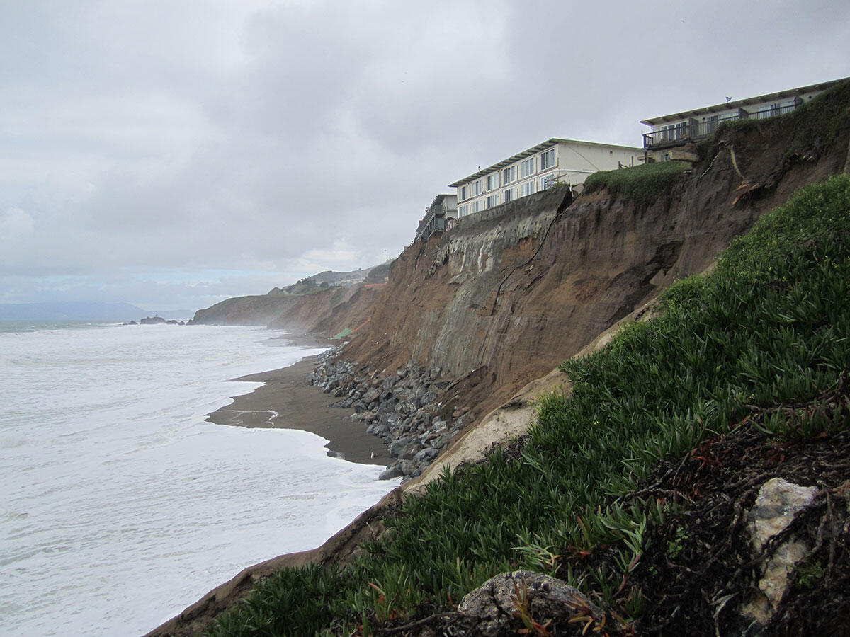 Photo of a coastal cliff with an apartment building right at the edge of the cliff.