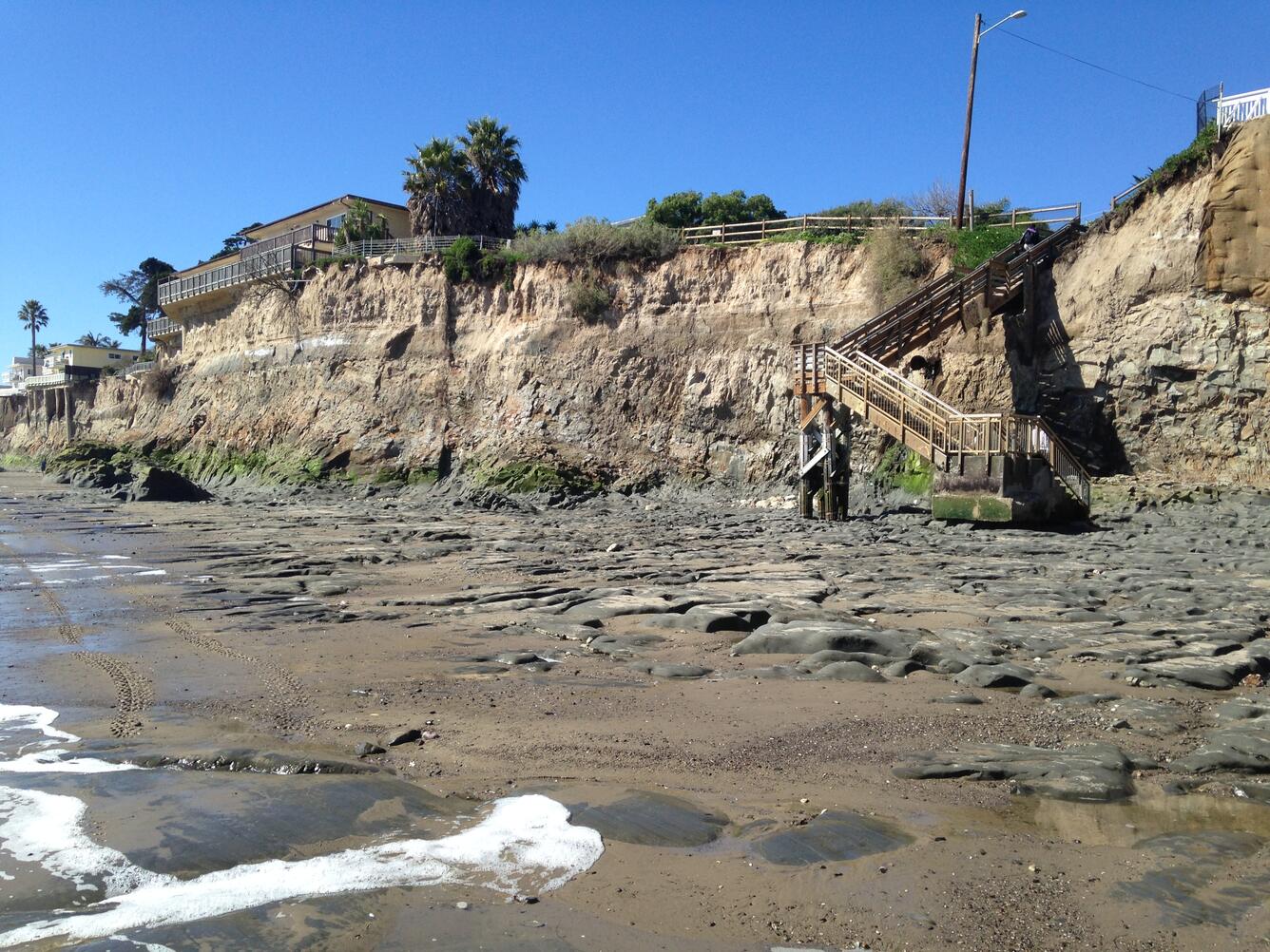 house perched at the top of cliff edge above beach.