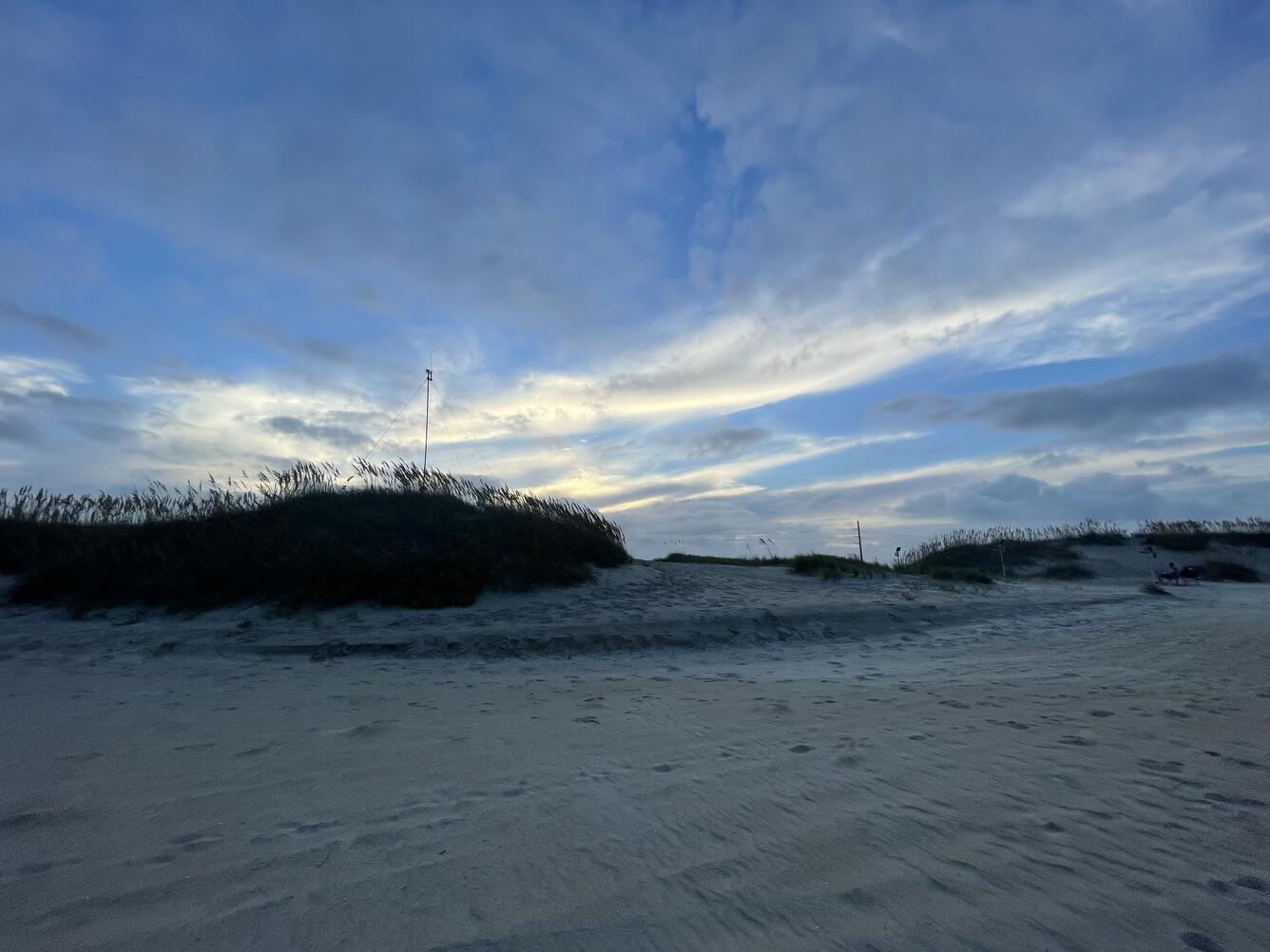 Photo looks at beach dunes from the sandy part of the beach, and a pole with an antenna on top stands on the dune.