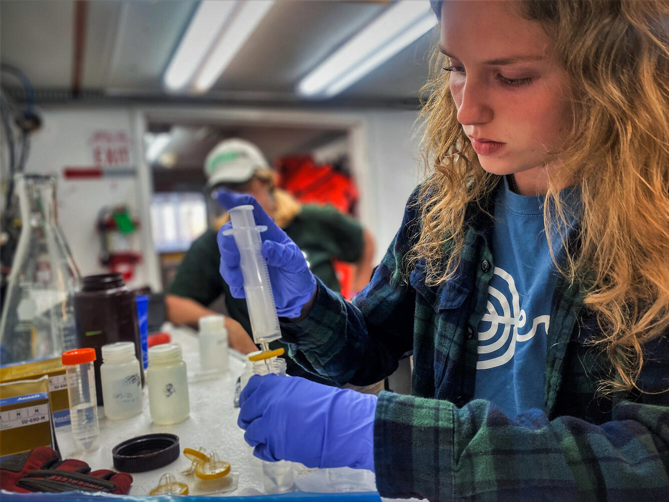 a girl wearing gloves holding a pipette in a lab