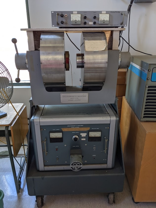 Two metal drums are held vertically above a steel-cased box. Perched on top, an instrument panel's dials look on disapprovingly.