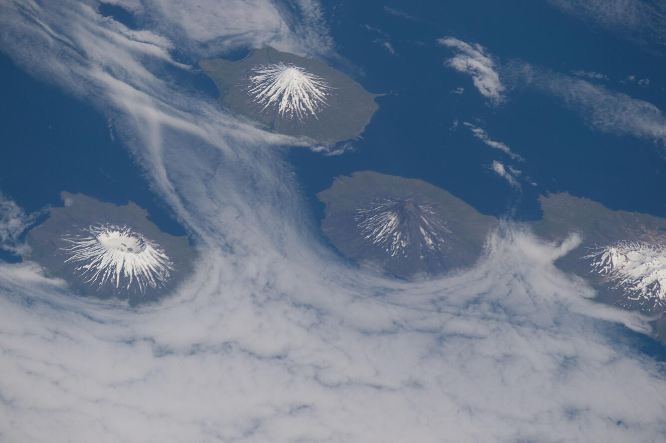 Photograph of four volcanoes surrounded by clouds and ocean taken from space