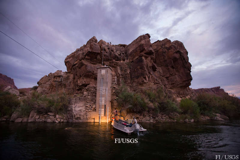 A boat on the Colorado River in front of a rock outcrop containing a concrete structure. 