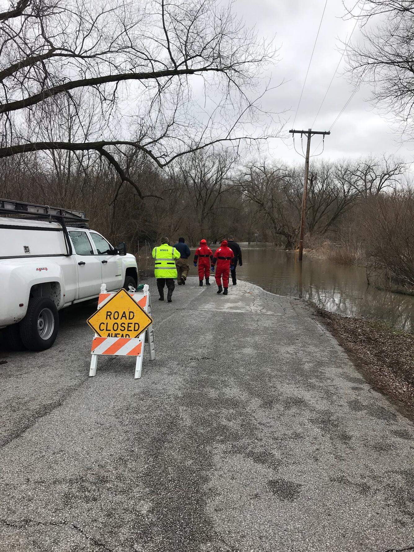 USGS hydrographers stands near a flooded river and prepare to make a discharge measurement to see how much water is flowing. 
