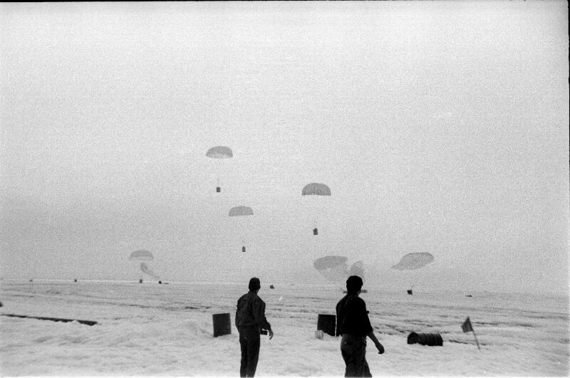 Black and white image shows supplies being parachuted into an ice field