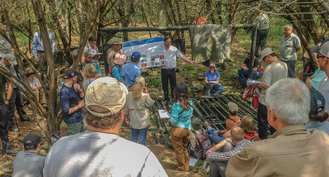 Overhead view of attendees gathered at Friesenhahn Cave.  Presenter and locked cave entrance visible at center.