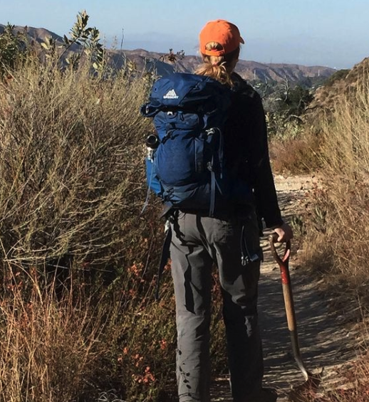 person with hiking gear walking away from camera on a grassy trail