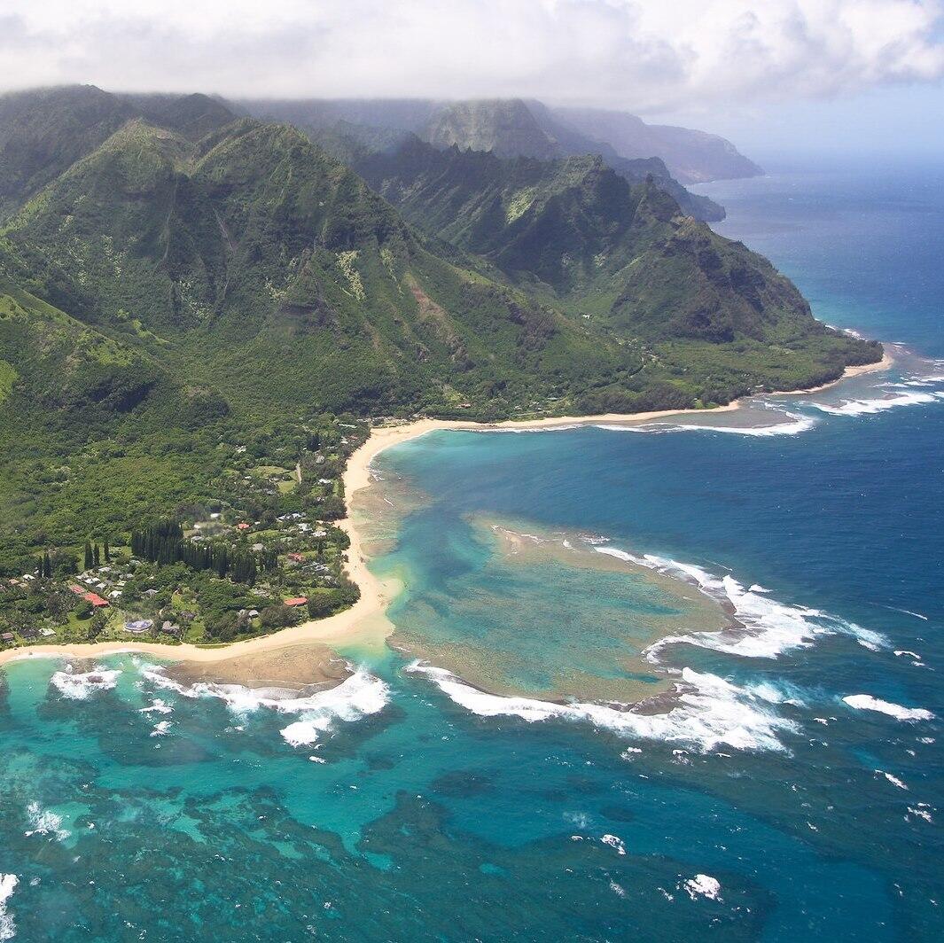An aerial view of the Island of Kaua'i, with lush green mountains and turquoise waters meeting the coastline